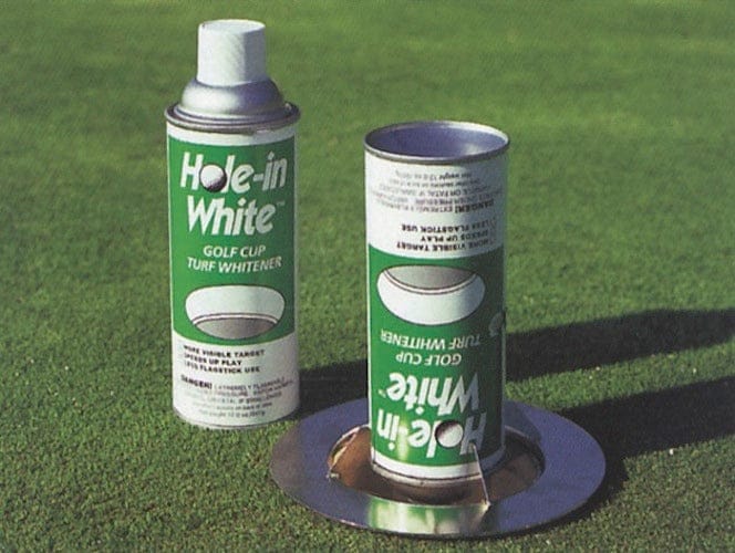 Grüne Dose mit weißer Markierungsfarbe neben passendem Deckel auf Golfplatzgras.