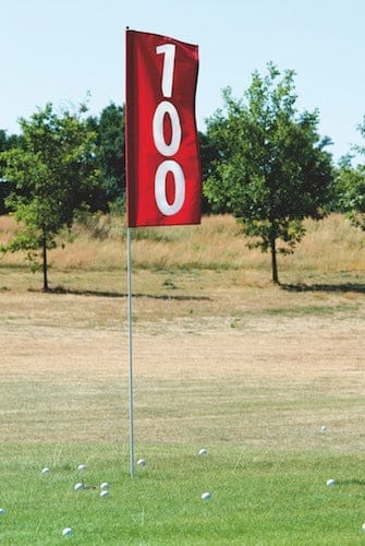 Rotes Fahnenbanner mit weißer Zahl 100 auf Metallstab im Golf-Driving-Range-Hintergrund.