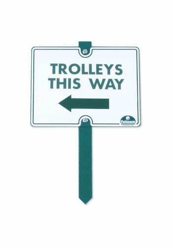 Weißes rechteckiges Schild mit grünem Rand, grünem Text "Trolleys This Way" und linkem Pfeil auf grünem Erdspieß.