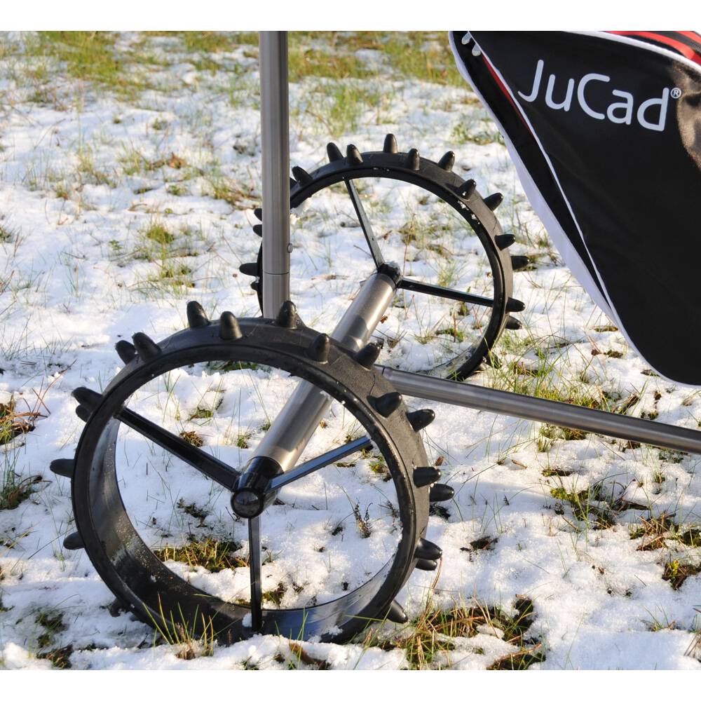 Schwarze Jucad Winterreifen mit grobem Profil auf Golf-Trolley bei Schnee und Gras.
