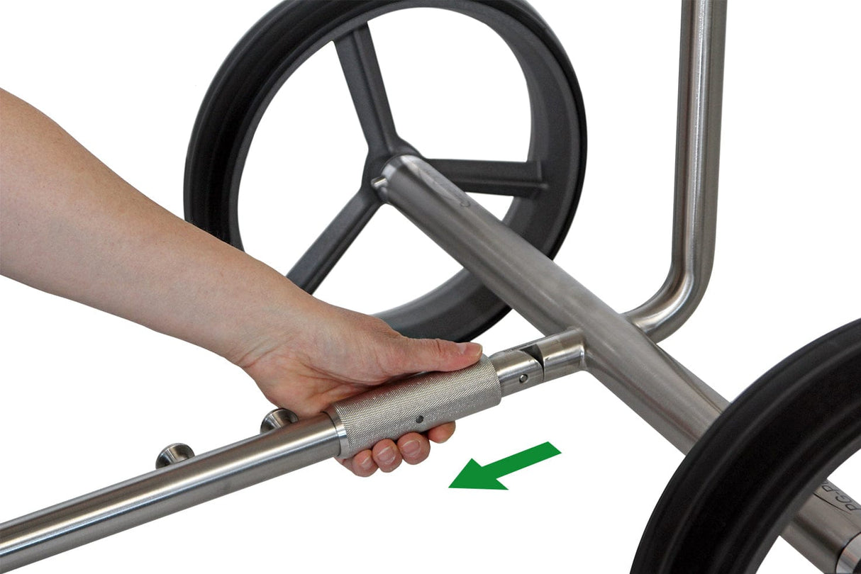 Hand schiebt grauen Stahlrohrgriff in Trolleyrahmen mit schwarzen Rädern, grüner Pfeil zeigt Einfügerichtung.