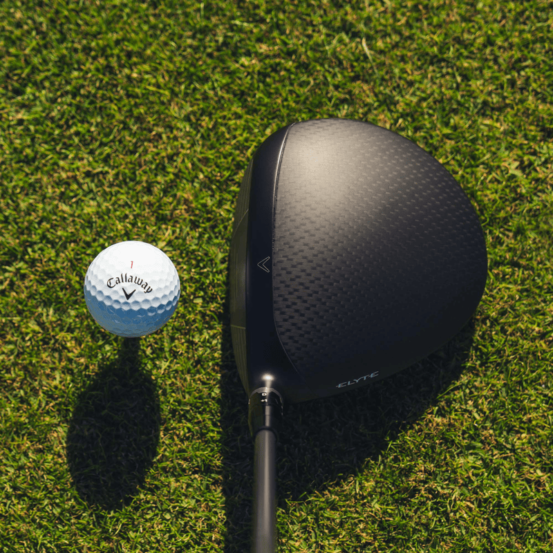 Schwarzer Callaway Elyte Driver mit matte Carbon-Oberfläche neben weißem Golfball auf grünem Grasspielfeld.